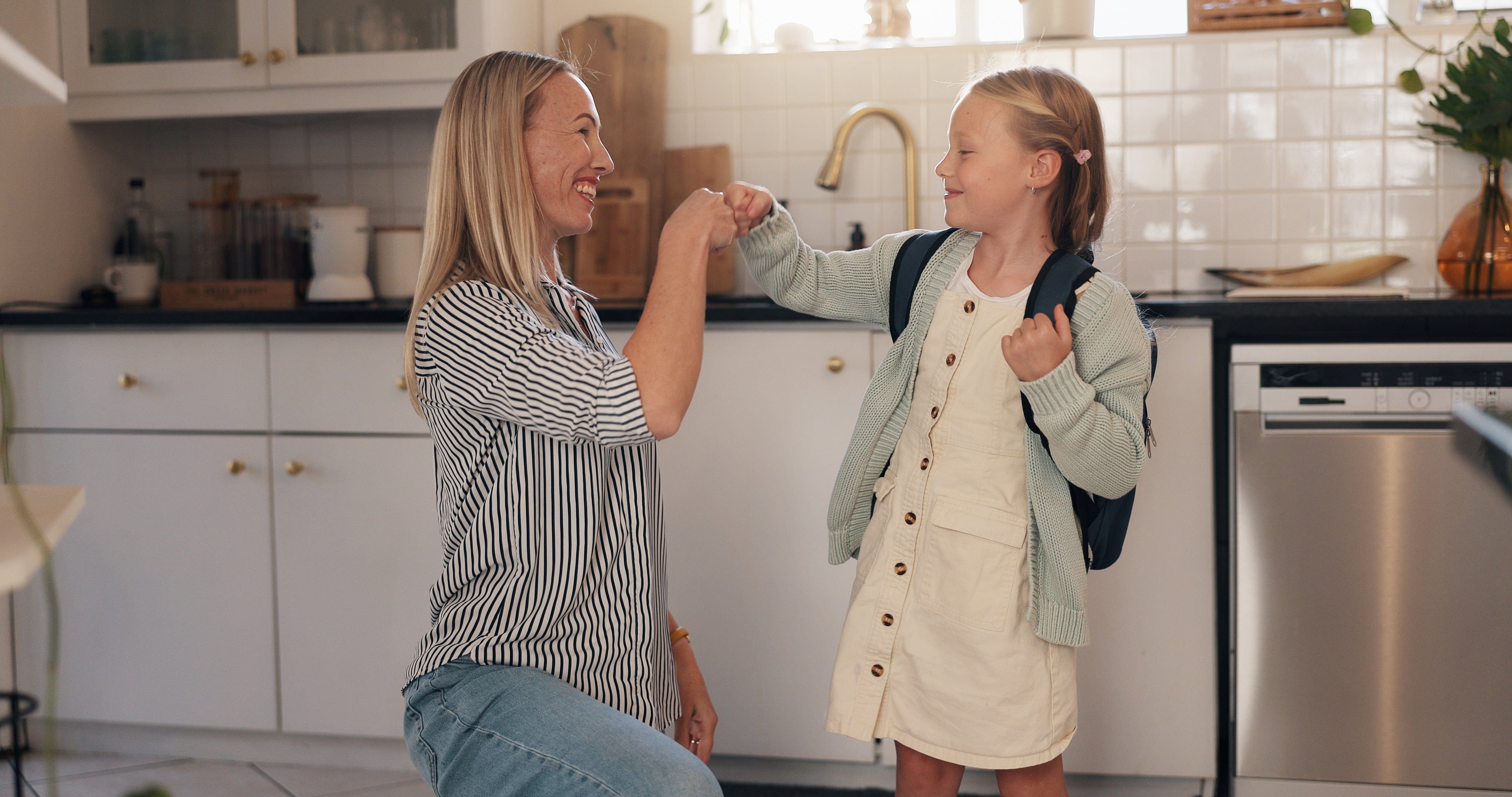 Woman and young girl in a kitchen with a backpack, indicating a school day.